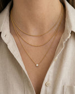 Two gold necklaces with a pearl pendant on a person wearing a light-colored shirt.