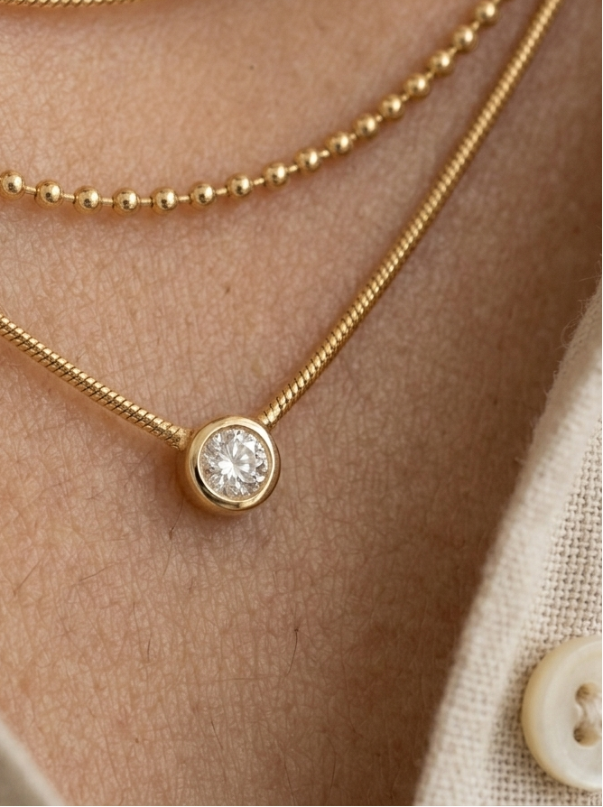 Close-up of a person wearing multiple gold necklaces with a focus on a diamond pendant.