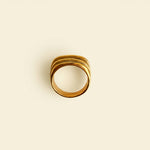 Gold ring on a light gray surface with a beige jewelry box in the background
