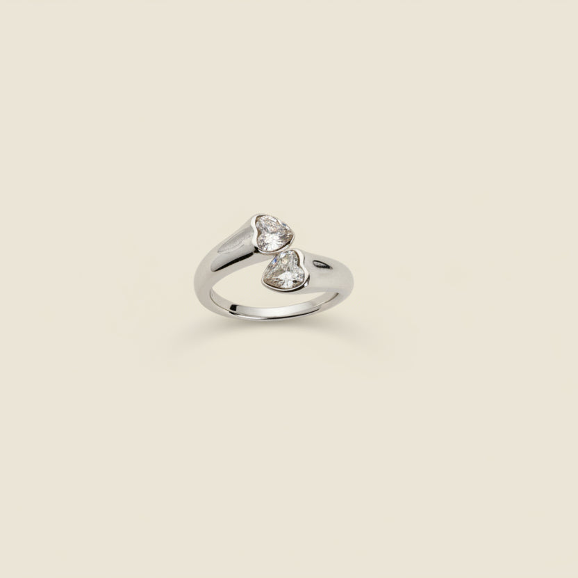 Silver ring with heart design on a beige cylindrical stand against a light background