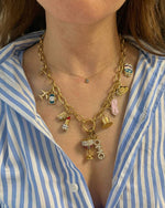 Gold charm necklace with various charms worn by a person in a blue and white striped shirt.