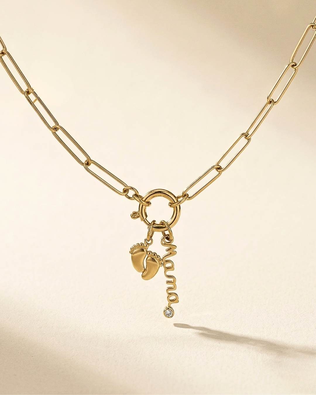 Gold necklace with foot charm and 'Mum' pendant on a beige background
