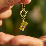Hand holding a necklace with a green coffee cup charm against a blurred green background