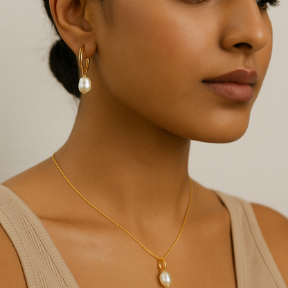 Close-up of a woman wearing gold earrings and necklace with pearl accents on a neutral background