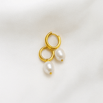 Gold hoop earrings with pearl drops on a light background