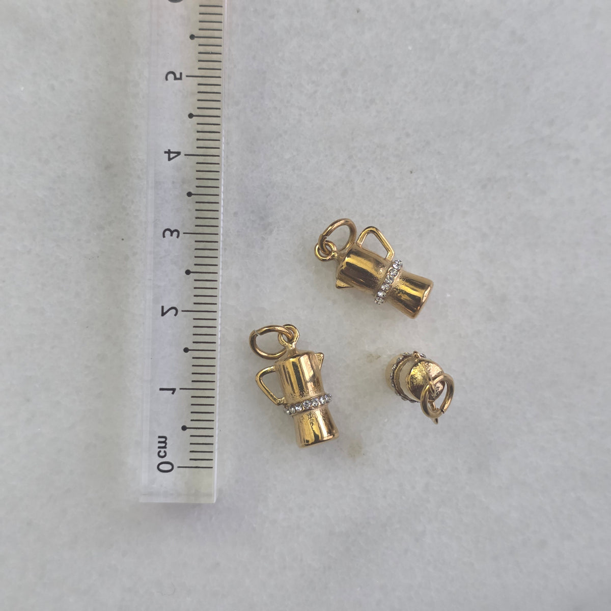 Gold charm shaped like a pitcher with a handle on a white background