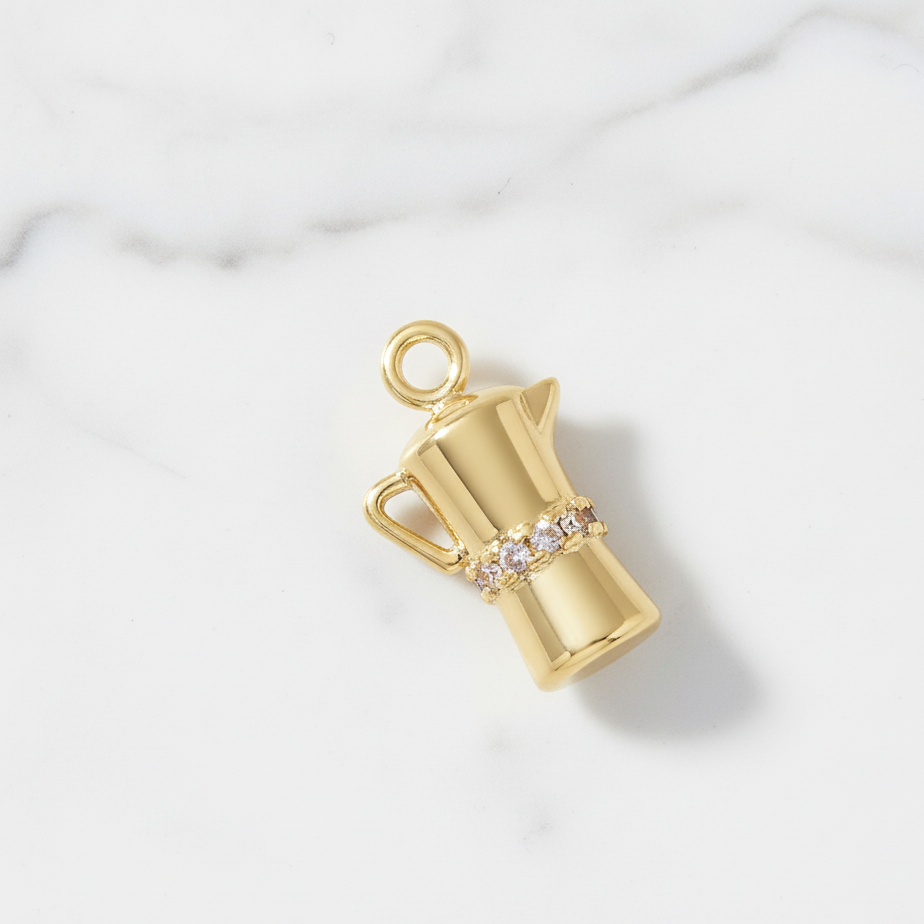 Gold charm shaped like a pitcher with a handle on a white background