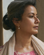 Woman wearing a pink traditional outfit with a beige shawl, looking to the side.