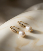 Pair of pearl earrings on a textured beige surface