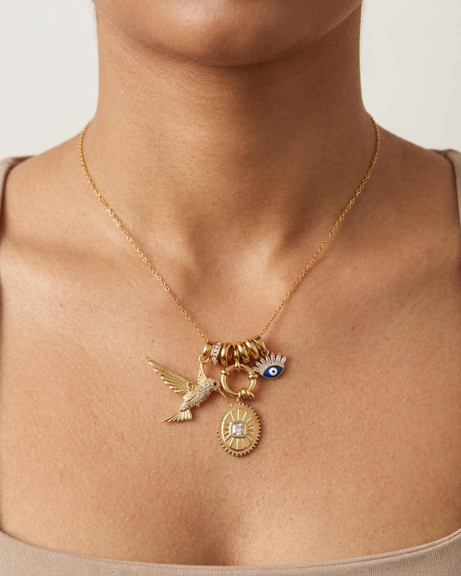 Gold necklace with charms on a person wearing a beige top against a neutral background