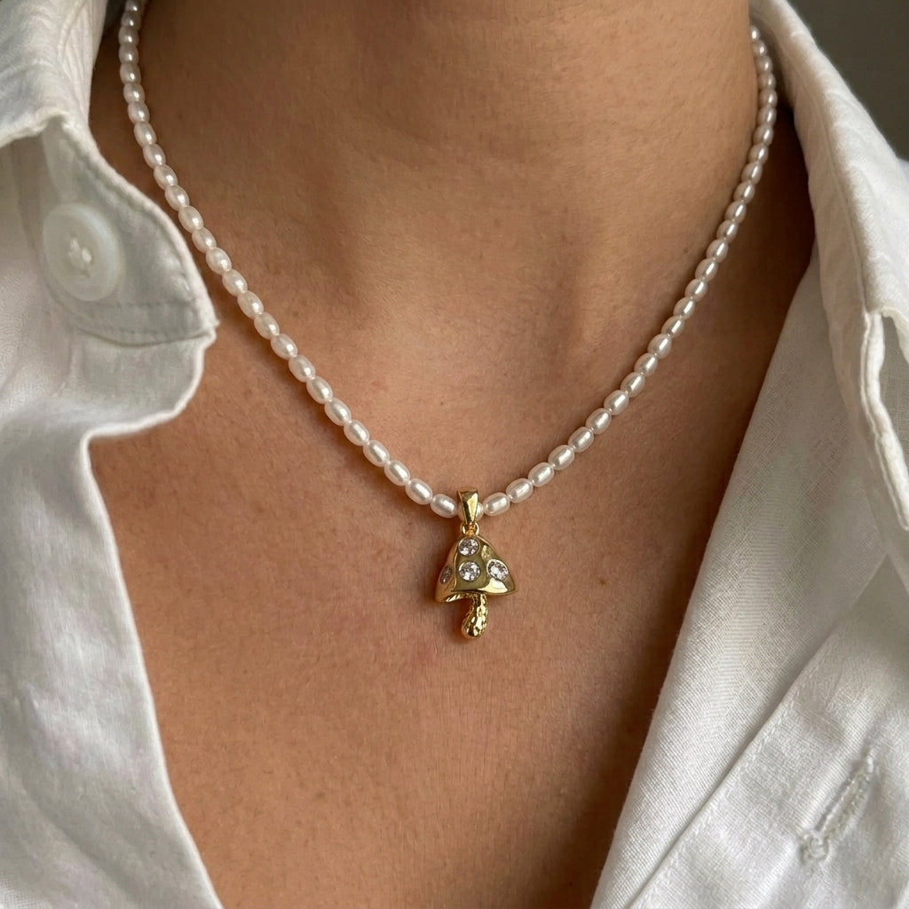 Pearl necklace with a gold mushroom pendant worn by a person in a white shirt.