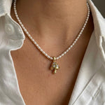 Pearl necklace with a gold mushroom pendant worn by a person in a white shirt.