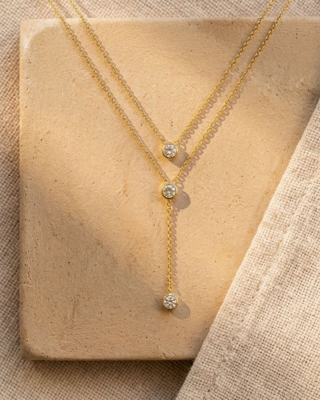 Gold necklace with diamond pendants on a beige stone surface