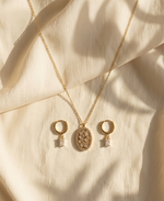 Gold necklace with three pendants on a beige fabric background
