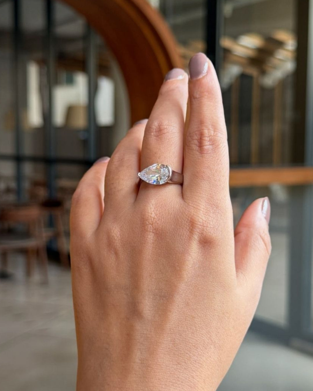 Hand wearing a diamond ring with a blurred indoor background