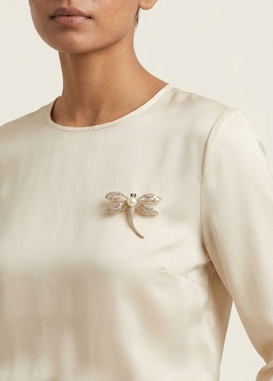 Woman wearing a beige sweater with a dragonfly brooch on a plain background
