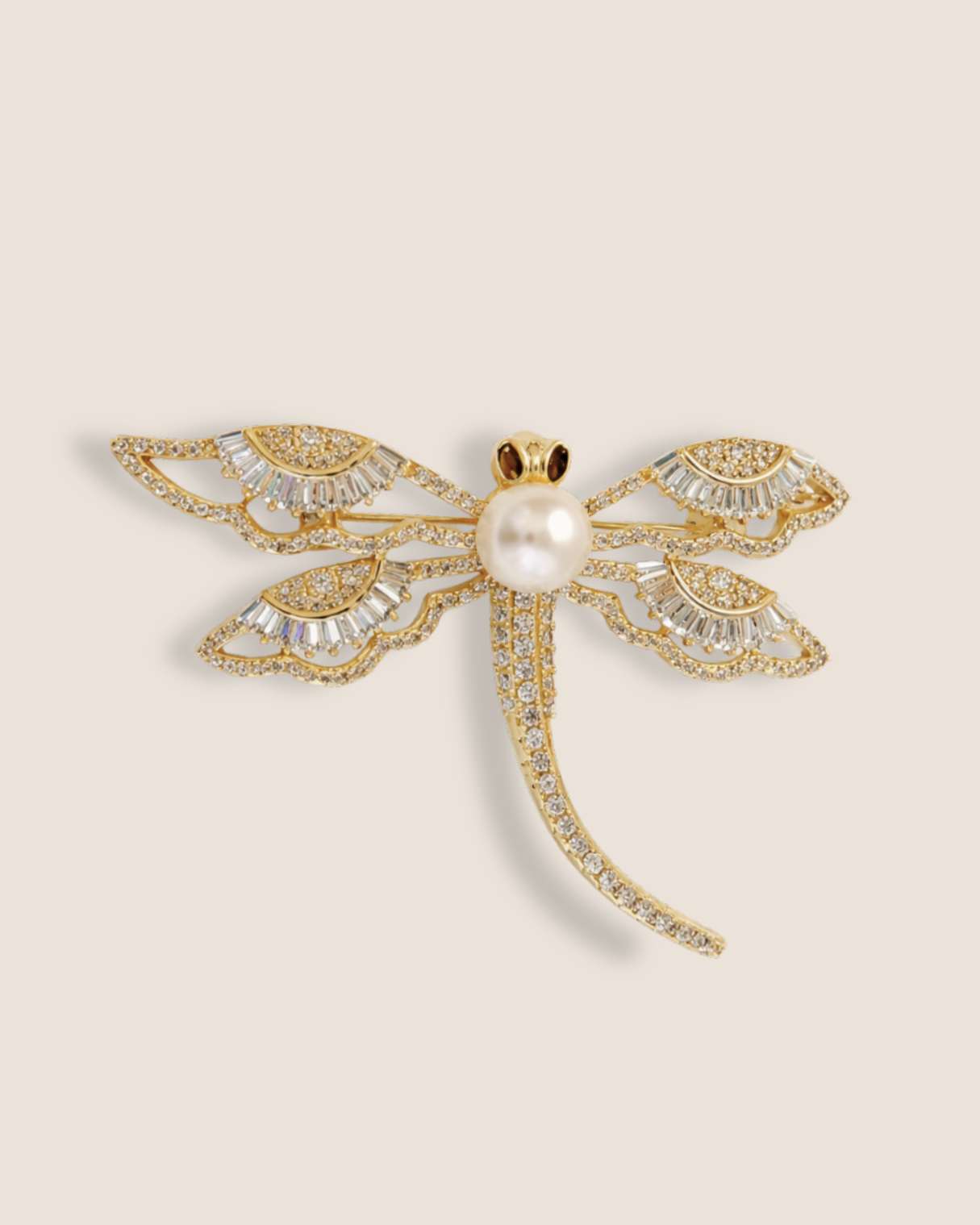 Gold dragonfly-shaped brooch with pearl center on a beige background