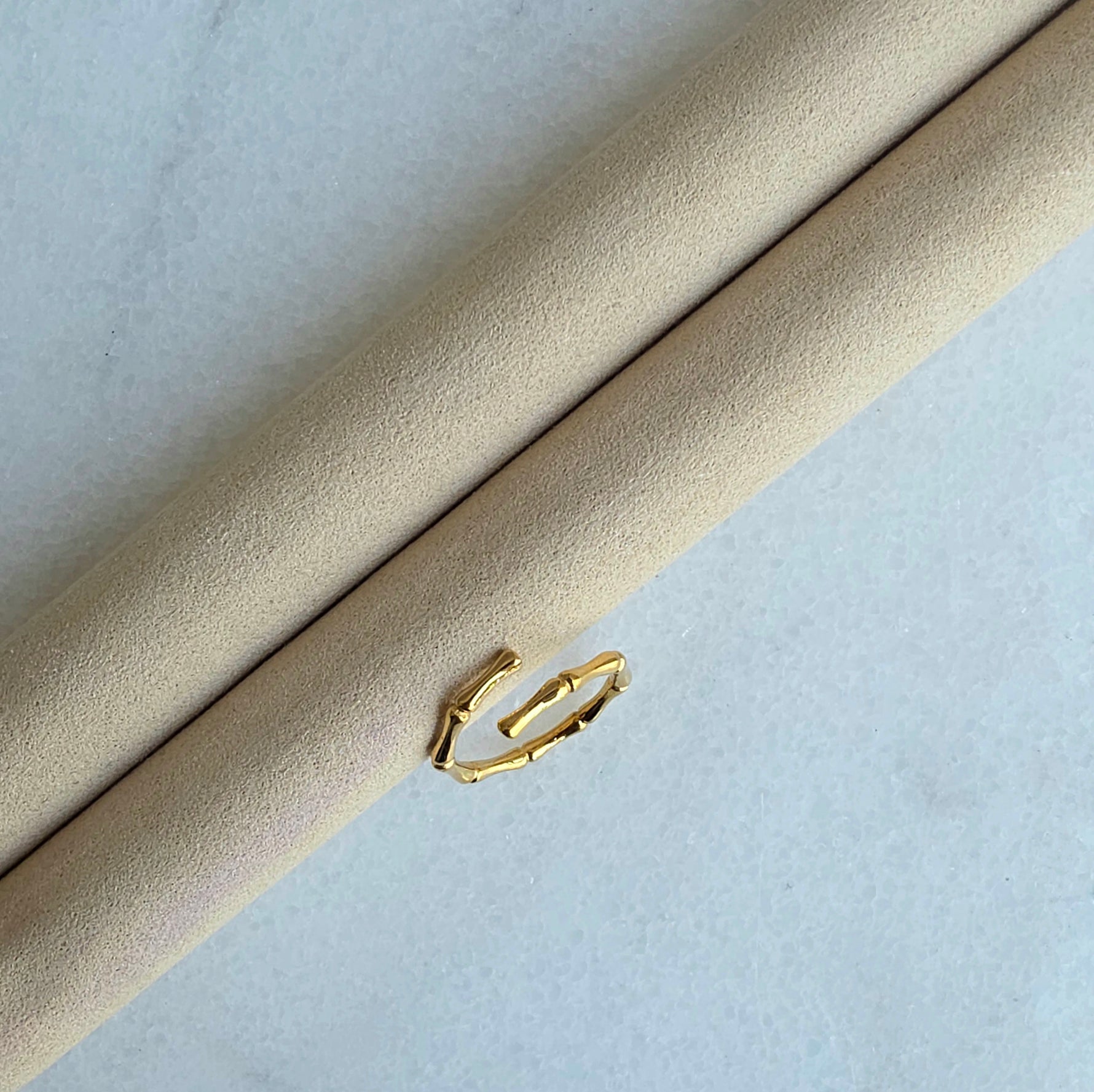 Gold hoop earring on a beige cushion against a light gray background