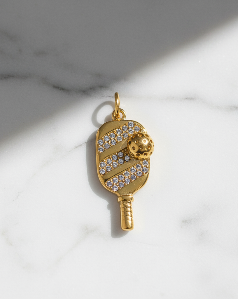 Gold pendant shaped like a paddle with a ball on a marble background