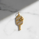 Gold pendant shaped like a paddle with a ball on a marble background