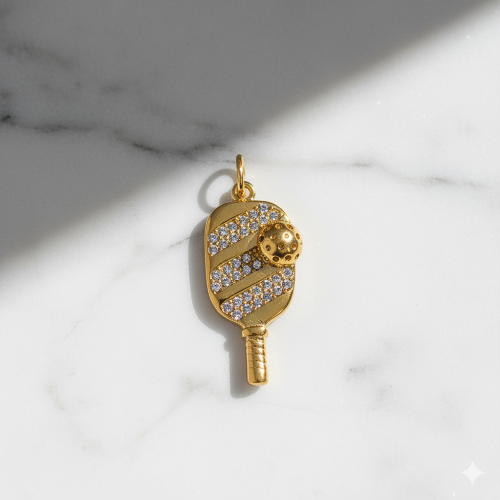 Gold pendant shaped like a paddle with a ball on a marble background