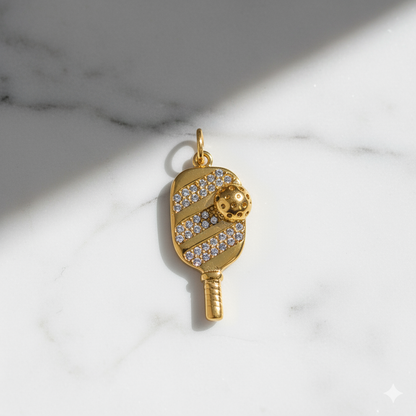 Gold pendant shaped like a paddle with a ball on a marble background