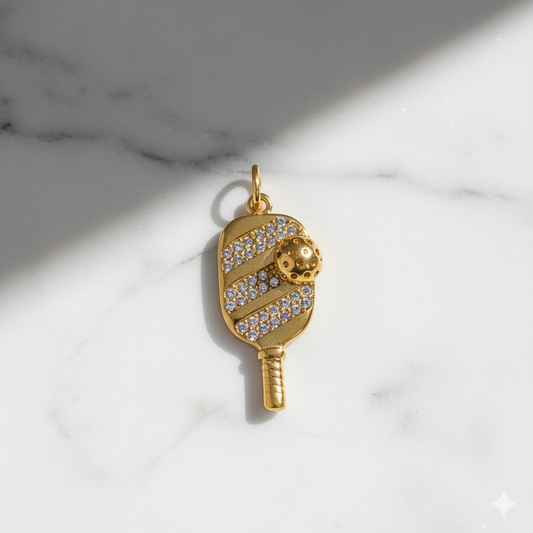 Gold pendant shaped like a paddle with a ball on a marble background