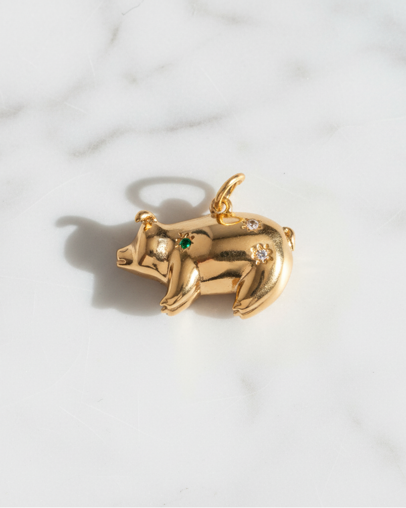 Gold pig-shaped pendant with green and clear gemstones on a marble background