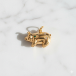 Gold pig-shaped pendant with green and clear gemstones on a marble background