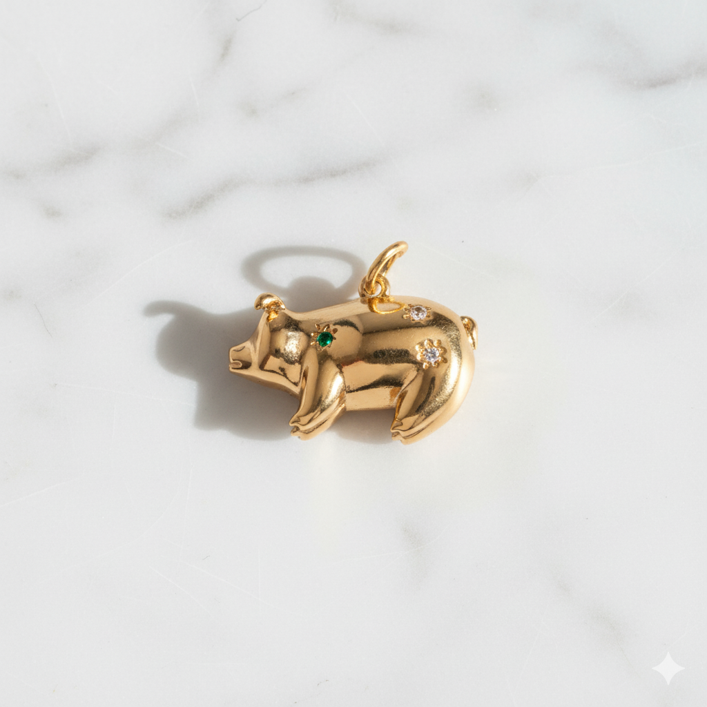 Gold pig-shaped pendant with green and clear gemstones on a marble background