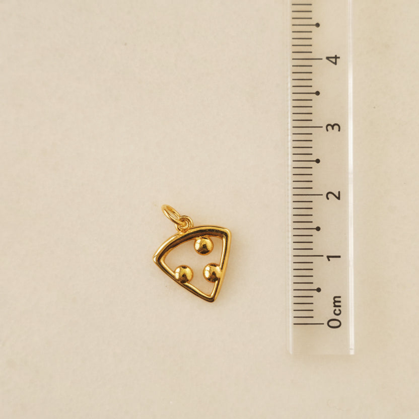 Gold triangular pendant on a gray background with a ruler for scale.