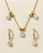 Gold jewelry set with teardrop-shaped crystals on a beige background