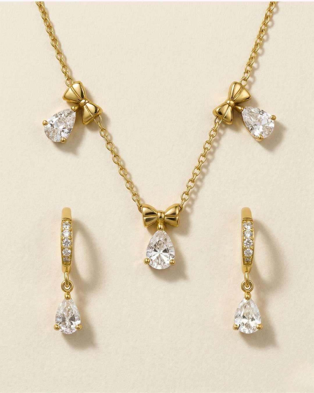 Gold jewelry set with teardrop-shaped crystals on a beige background