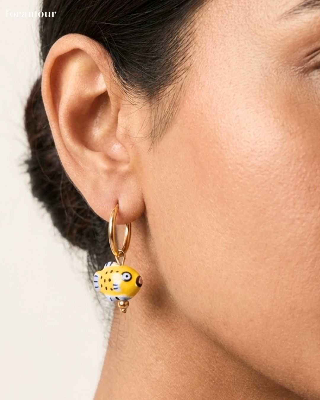 Close-up of an ear wearing a yellow and black patterned earring with a gold hoop.