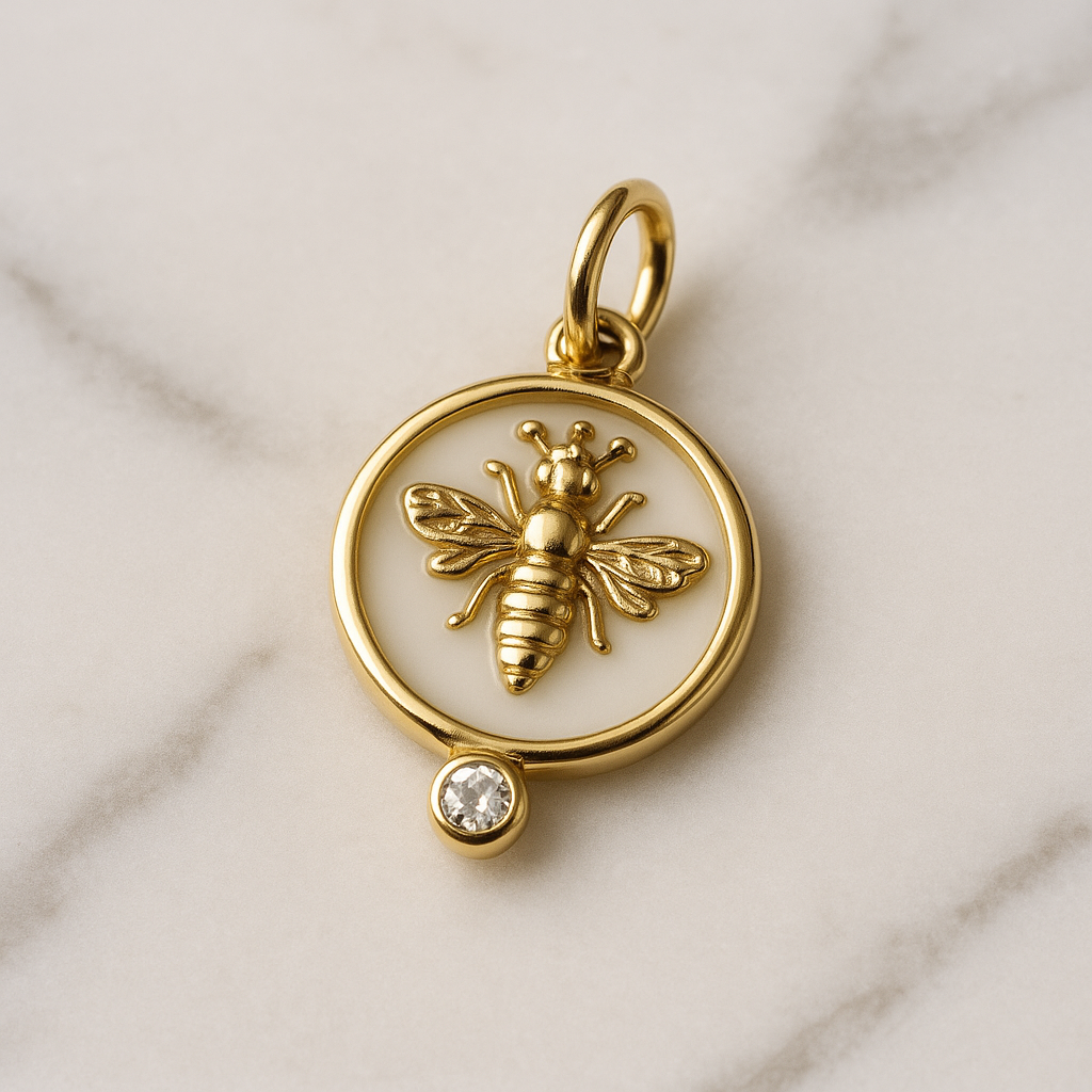 Gold pendant with bee design and small gemstone on a marble background