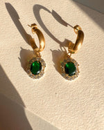 Gold hoop earrings with green gemstones on a beige surface