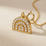 Gold rainbow-shaped pendant with diamonds on a beige background