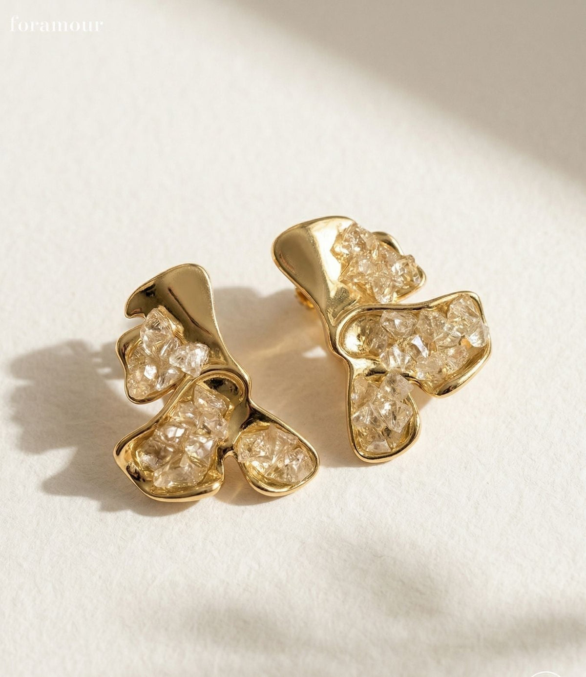 Gold earrings with clear gemstones on a light background
