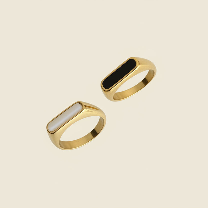 Two gold rings with black stones on a textured beige surface