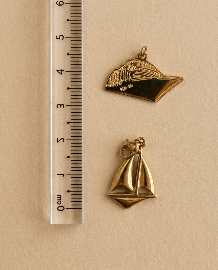 Two gold pendants on a beige background with a ruler for scale.