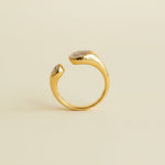Gold ring with gemstones on a textured beige and light gray background