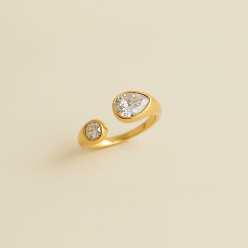 Gold ring with three diamonds on a beige cushion against a light gray background