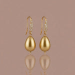 Gold earrings with teardrop-shaped pearls on a beige background
