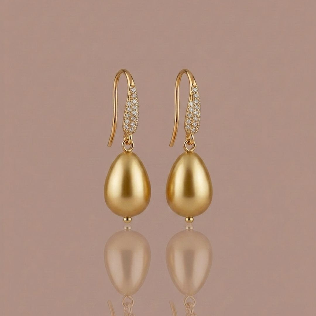 Gold earrings with teardrop-shaped pearls on a beige background