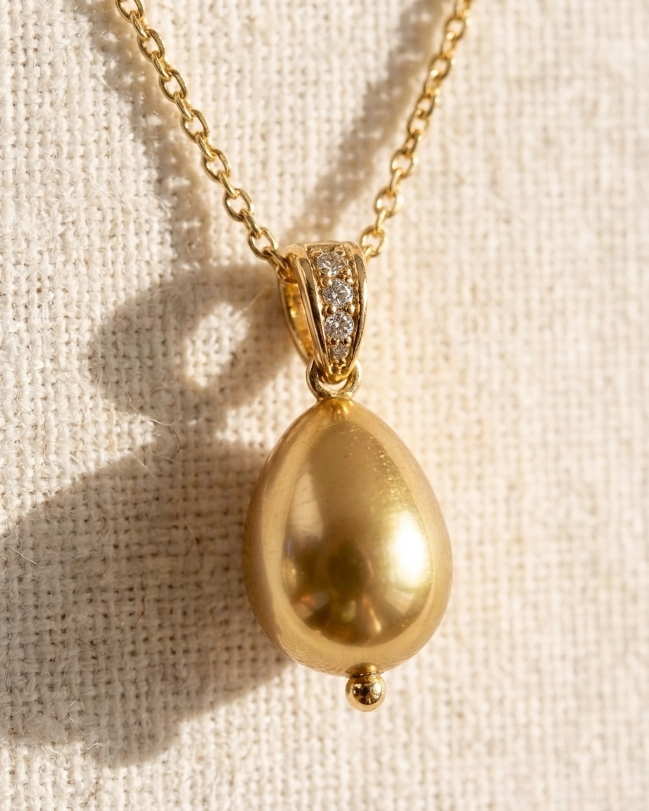 Gold teardrop pendant necklace on a textured beige background