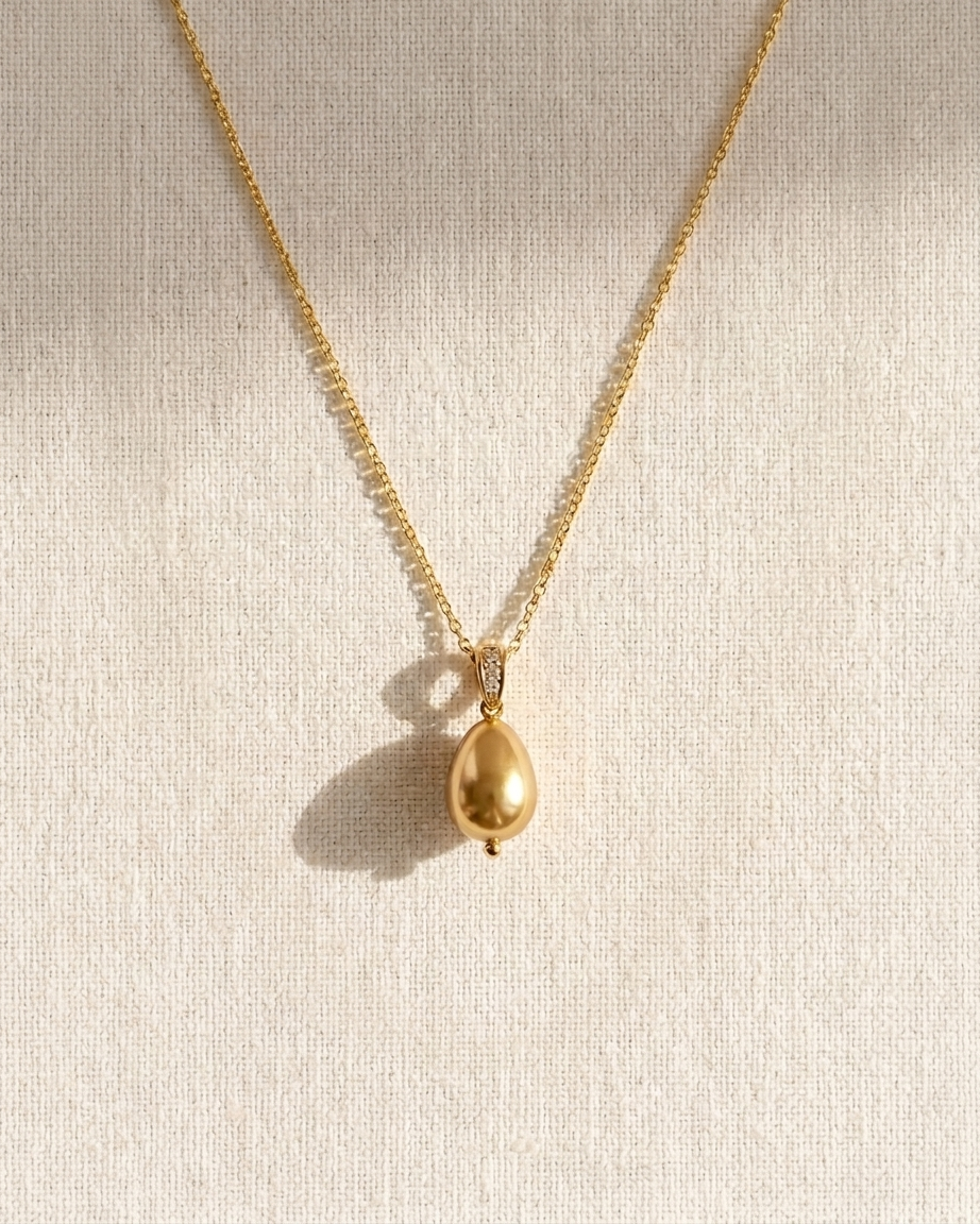 Gold necklace with a teardrop pendant on a beige background