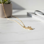Gold necklace with a leaf pendant on a light surface with a plant and book in the background