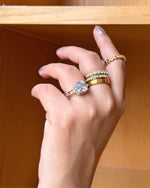 Hand wearing multiple gold rings with a wooden shelf in the background
