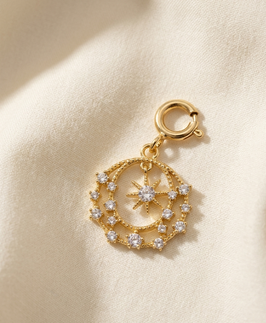 Gold charm with star and moon design on a beige fabric background