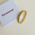 Gold bracelet on a white card with 'foramour' text on a marble surface